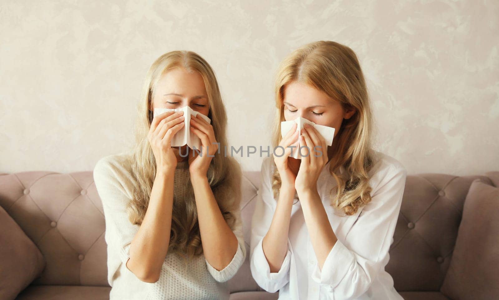 Sick exhausted middle-aged woman mother and adult daughter together sneezing blow nose using tissue at home