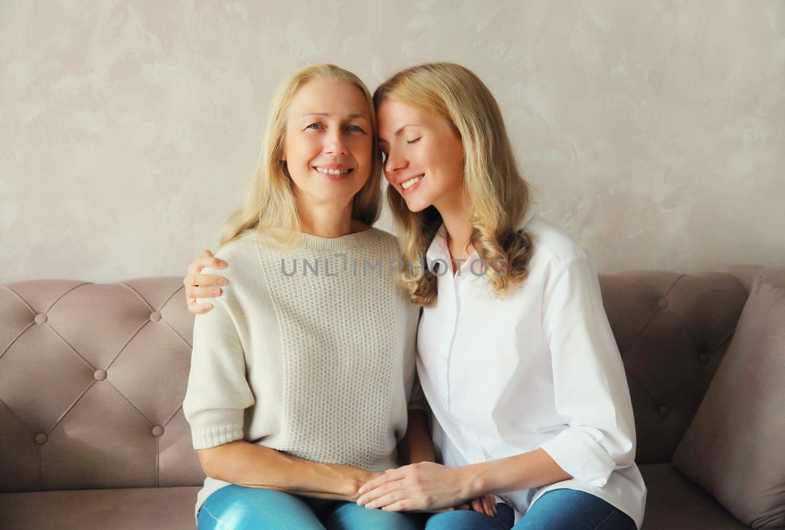 Portrait of happy smiling caucasian middle aged mother hugging her adult daughter together sitting on couch at home