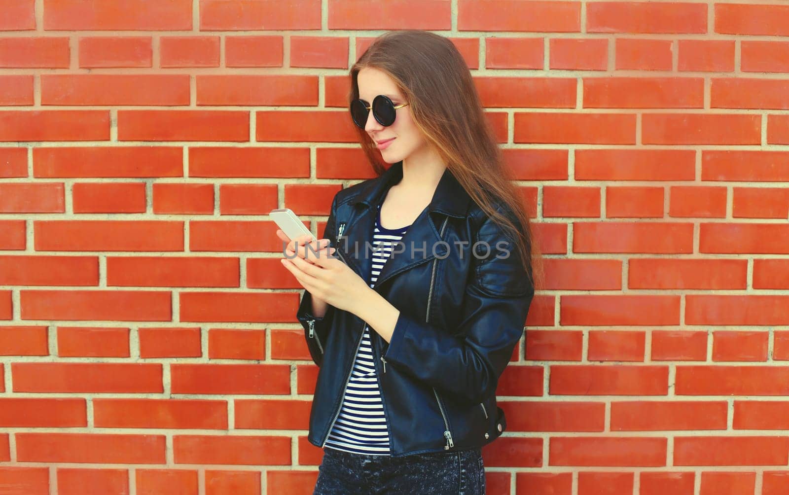 Modern caucasian young woman 20s model with mobile phone looking at device on city street
