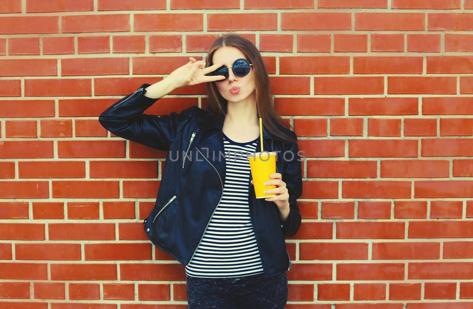 Portrait of stylish young woman model wearing black leather jacket in rock style on city street on brick wall background