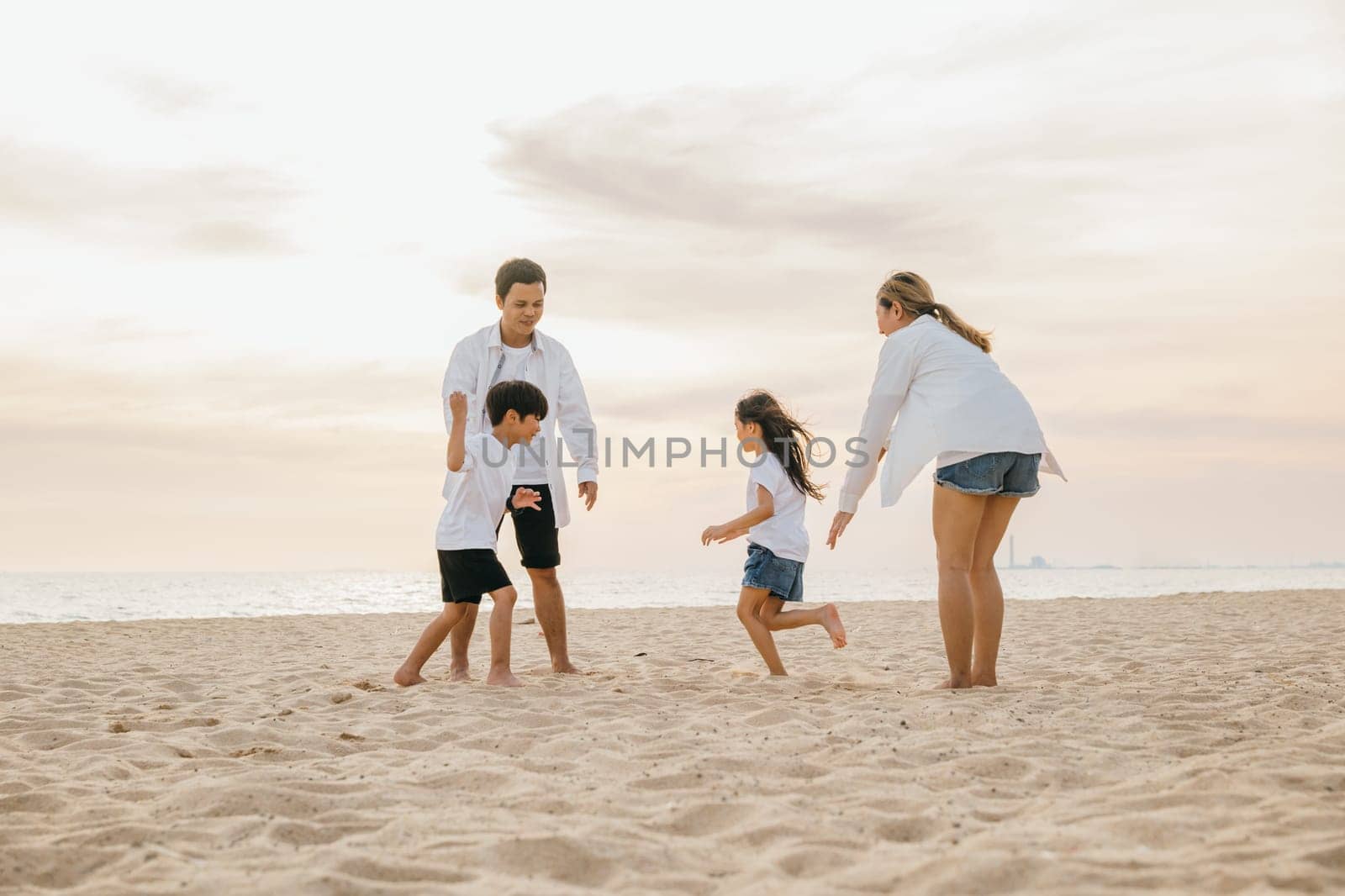A happy family enjoying a carefree day at the beach. Smiling father and mother with son and daughter running playing and laughing together. Summer holiday vibes with quality time and family bonding. by Sorapop