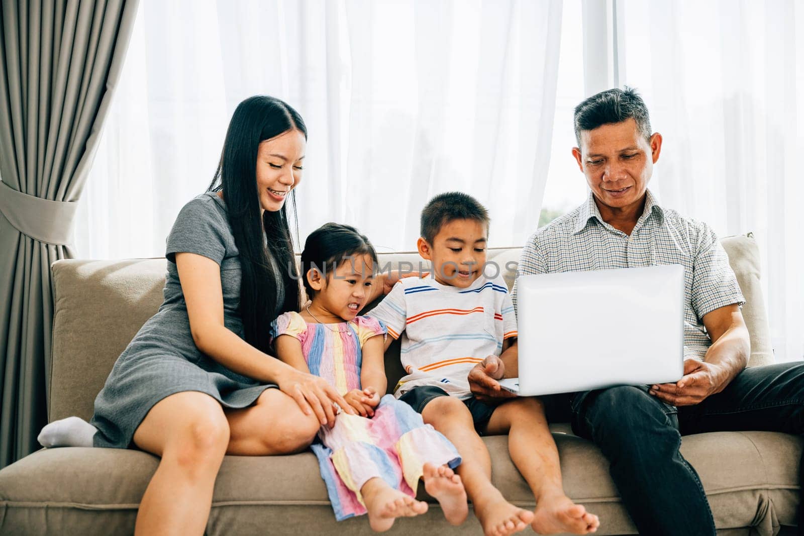 A cheerful family seated on a cozy sofa sharing a laptop parents and kids engaged in online browsing by Sorapop