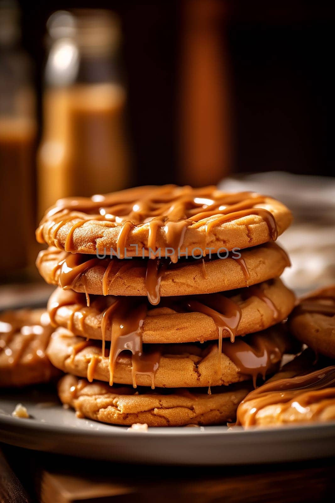 Stack of caramel drizzled pancakes on a plate with syrup bottles in background.