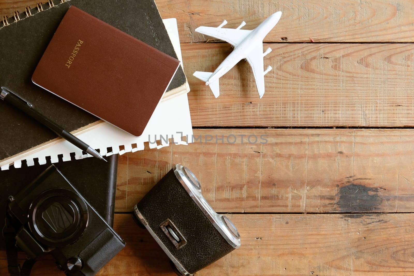 Travel concept with passport, camera, notebook and airplane on wooden background