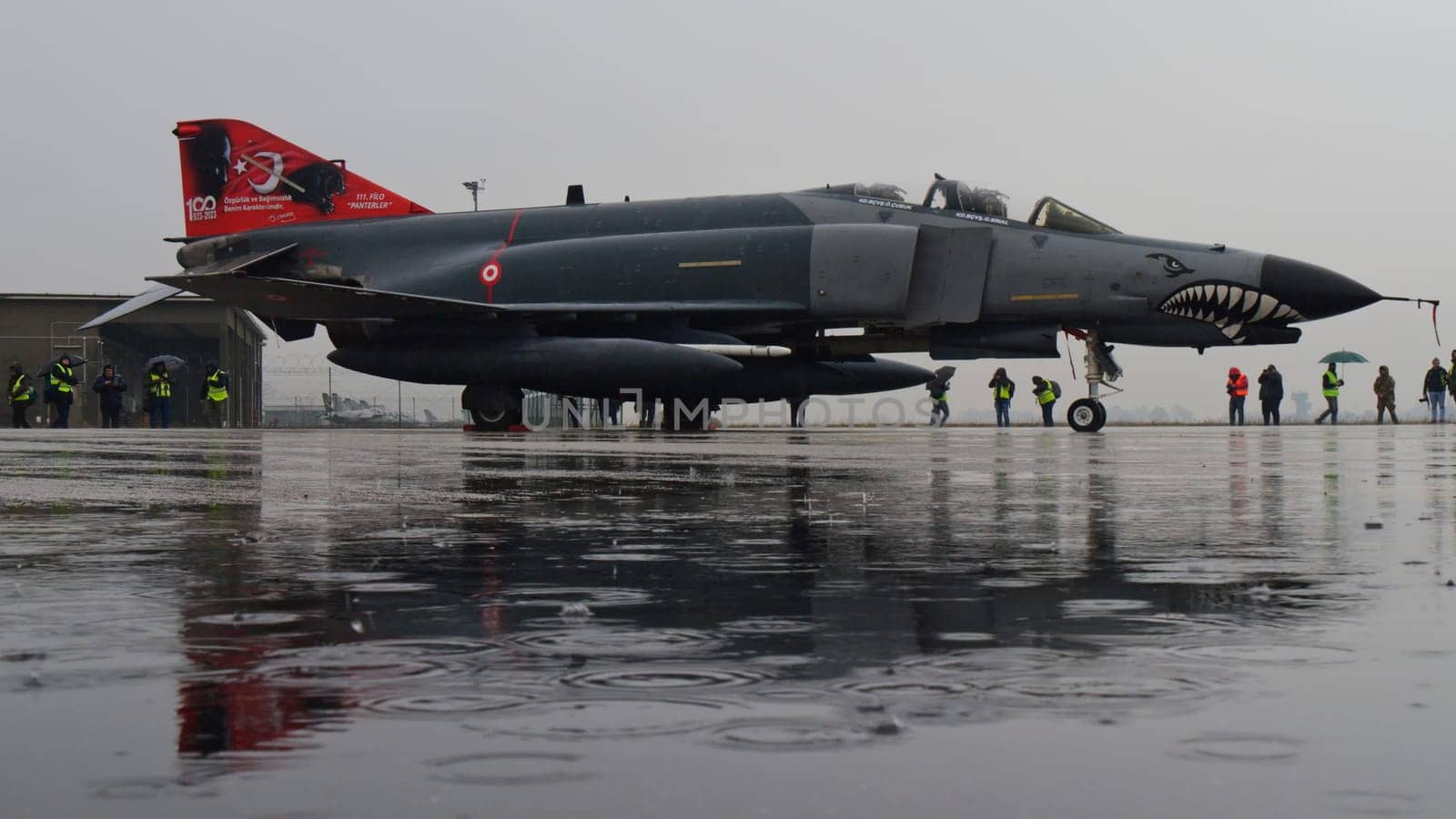 Turkish Phantom fighter jet, parked under the rain, casts its reflection on the water-saturated ground, merging the power of military aviation with the tranquility of nature. Copy space.