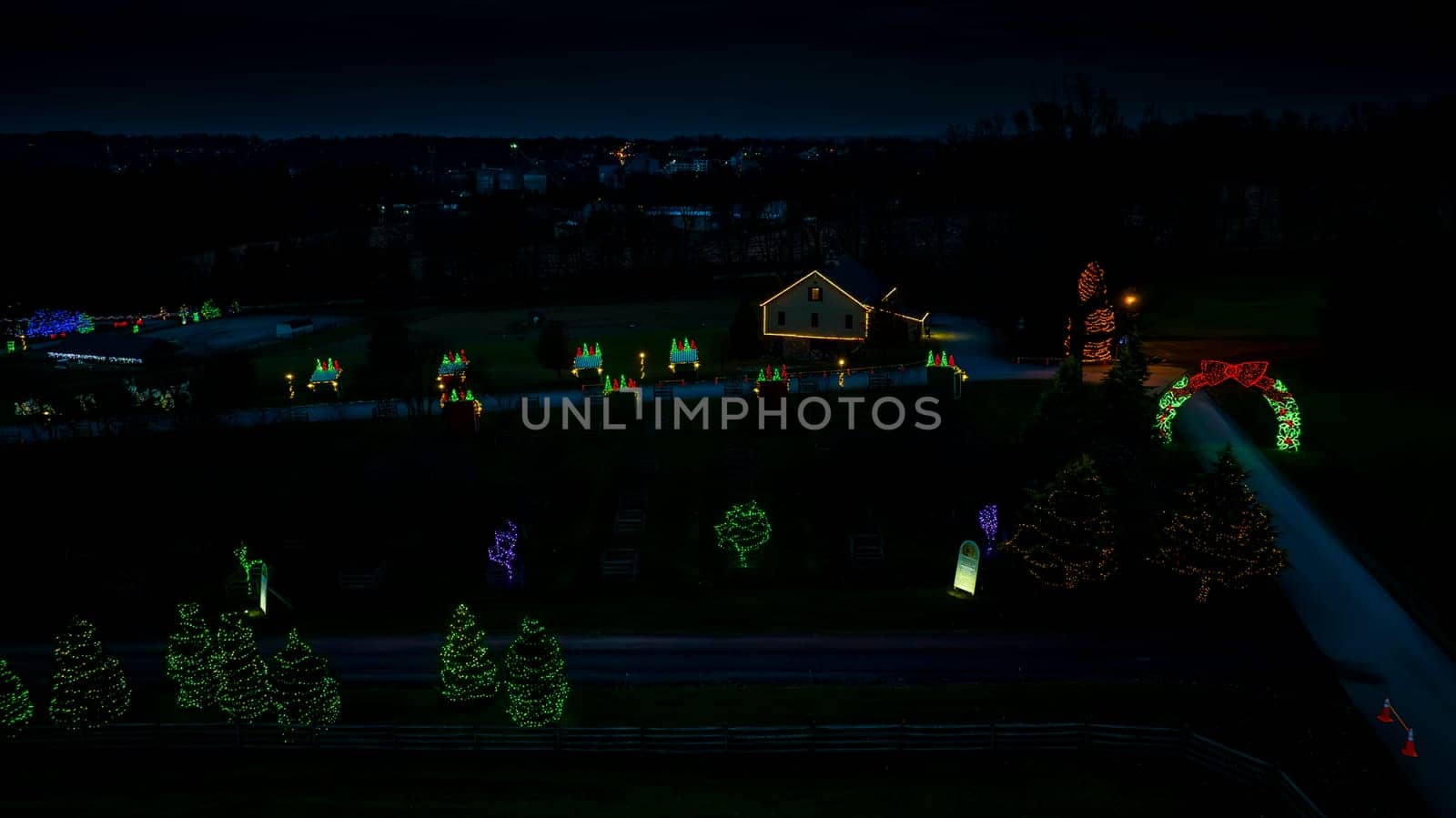 Twilight Scenery With Illuminated Christmas Decorations, Row Of Trees Wrapped In Lights, And A Lit House Against A Dusky Sky.