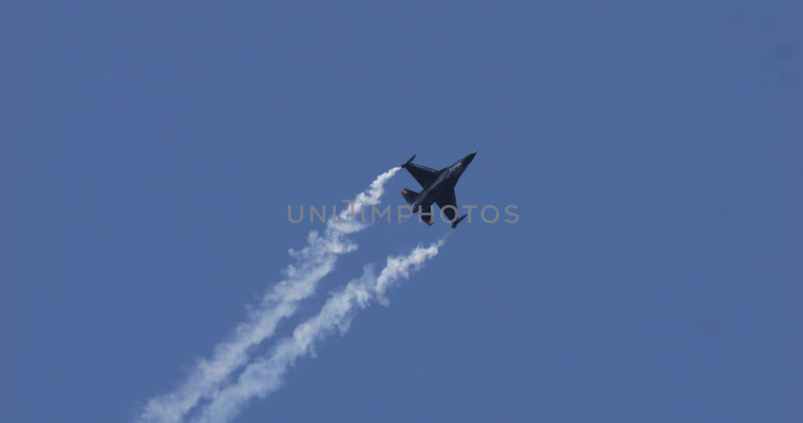 Mollis Switzerland August 19 2023: Silhouette of a fighter jet dominates the blue sky, marked by dramatic smoke trails from its wingtips. Belgian F-16 Fighting Falcon. Copy Space.