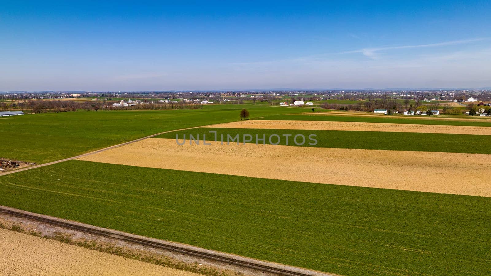 Vast Agricultural Fields With Distinctive Green And Beige Patterns Bordering A Small Town Under The Expansive Blue Sky.