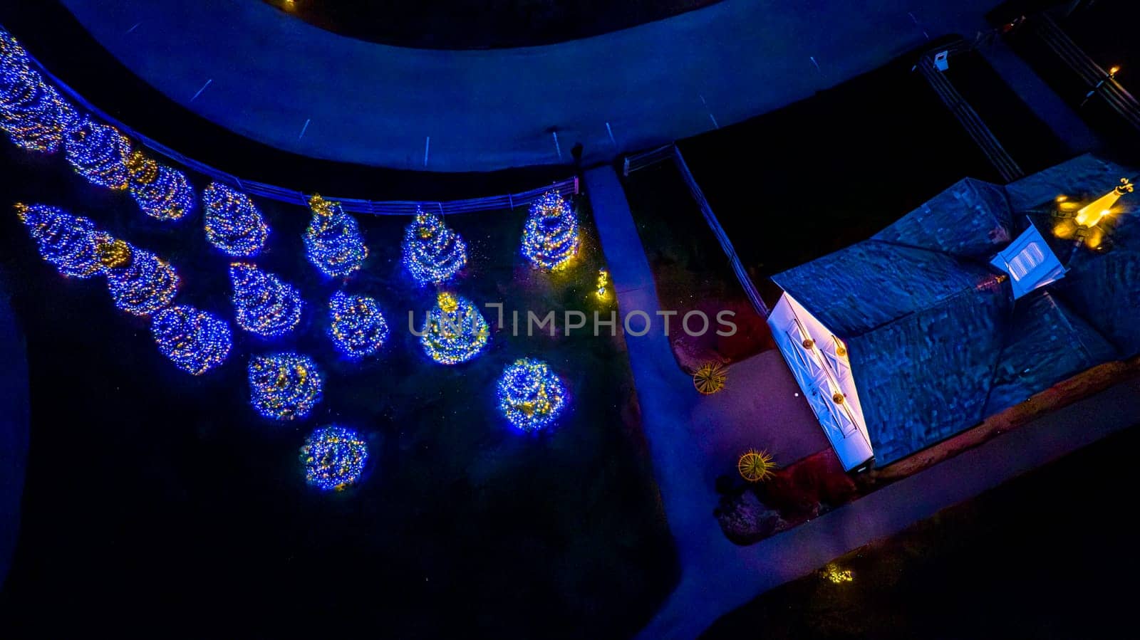 Aerial Nighttime View Of A Curved Path Lined With Illuminated Trees Resembling A String Of Pearls Next To A Structure With A Lit Entrance.