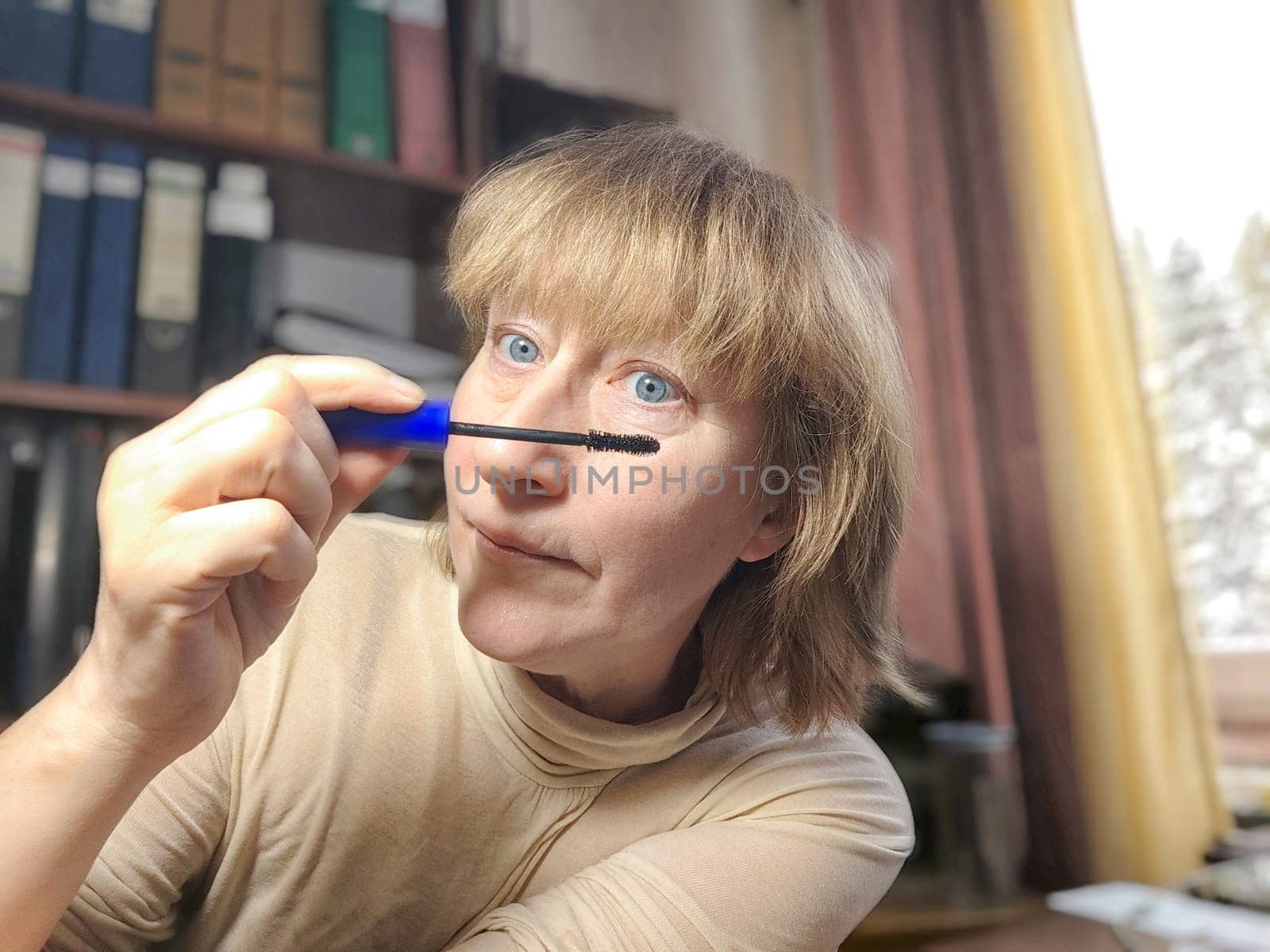 Portrait of a middle-aged woman doing eye makeup. Selfie portrait of lady who is businesswoman, accountant, manager, freelancer doing morning makeup at office on working place