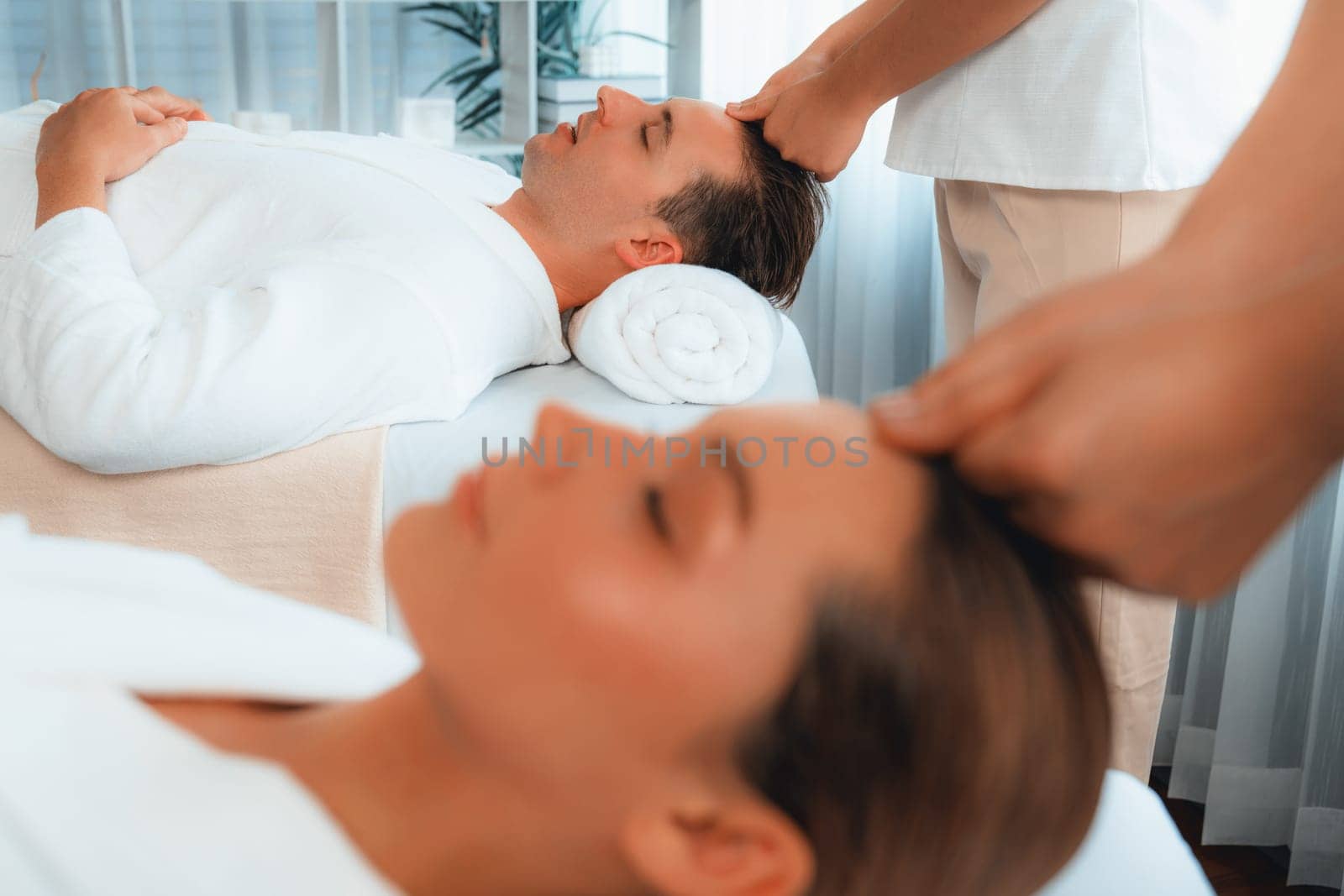 Caucasian couple enjoying relaxing anti-stress head massage and pampering facial beauty skin recreation leisure in dayspa modern light ambient at luxury resort or hotel spa salon. Quiescent