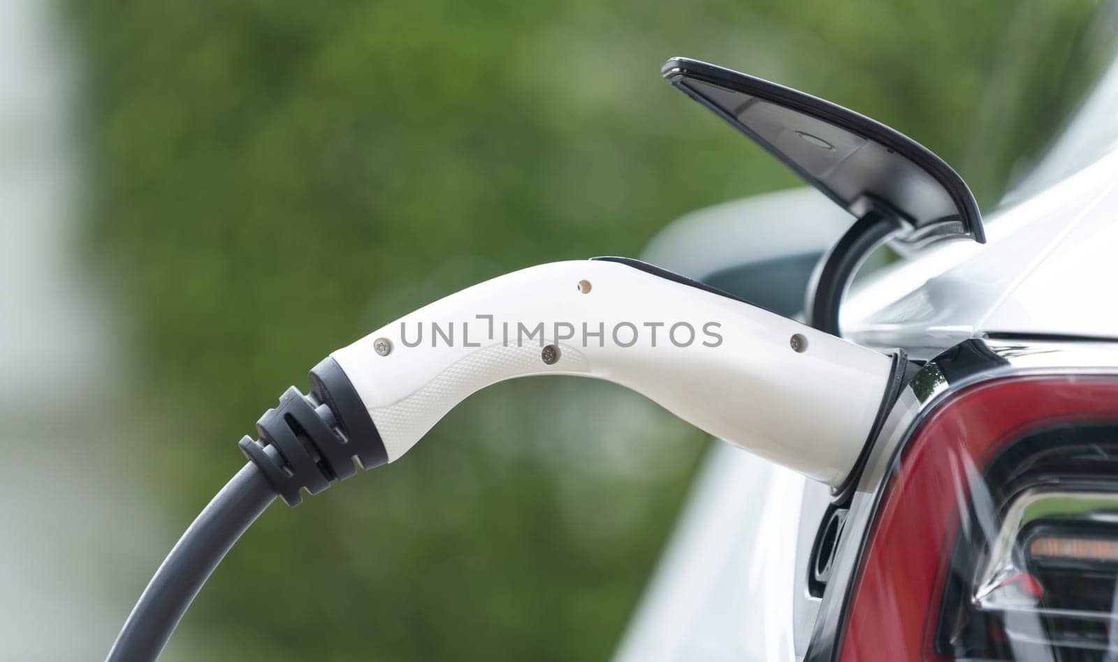 Closeup EV charger plug handle attached to electric vehicle port, recharging battery from charging station. Modern designed EV car and clean energy sustainability for better future.Panorama Synchronos