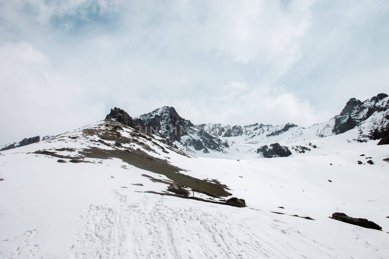 Snow-capped mountain peaks and rocks in the distance with snow-covered hills in the foreground by Pukhovskiy