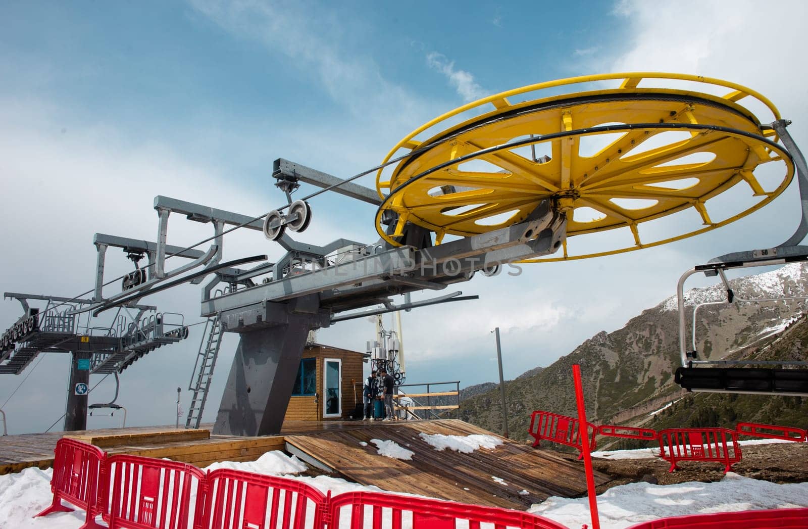 Yellow and gray ski lift wheel and tower with a blue sky and snow-capped mountains in the background by Pukhovskiy