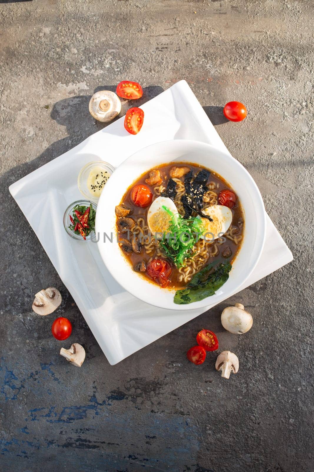 A flavorful ramen bowl with veggies, mushrooms, egg, noodles. Rich broth, topped with mushrooms, tomatoes, green onions. Served with boiled egg, lemon. Satisfying warming