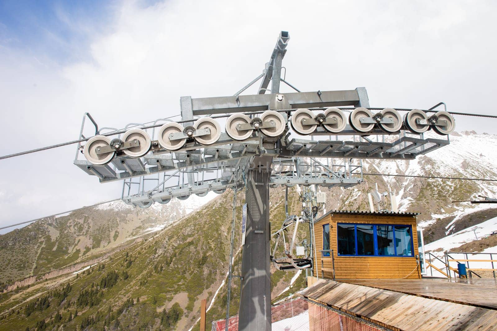 Yellow and gray ski lift wheel and tower with a blue sky and snow-capped mountains in the background by Pukhovskiy