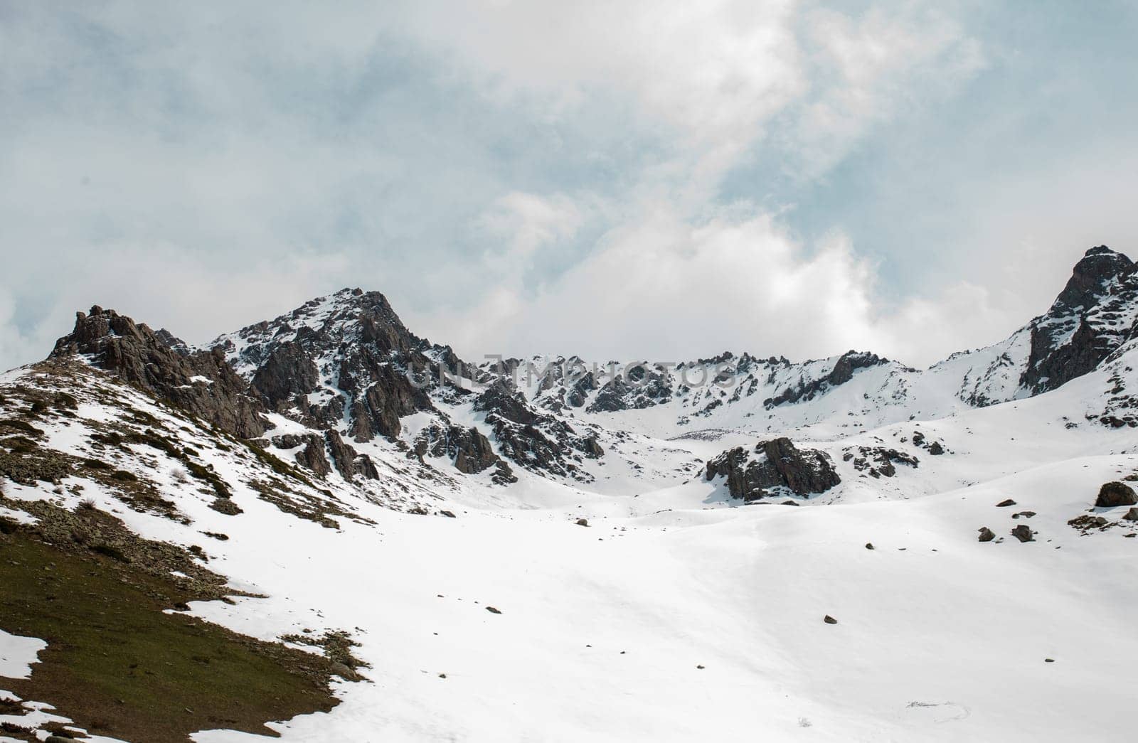 Snow-capped mountain peaks and rocks in the distance with snow-covered hills in the foreground by Pukhovskiy