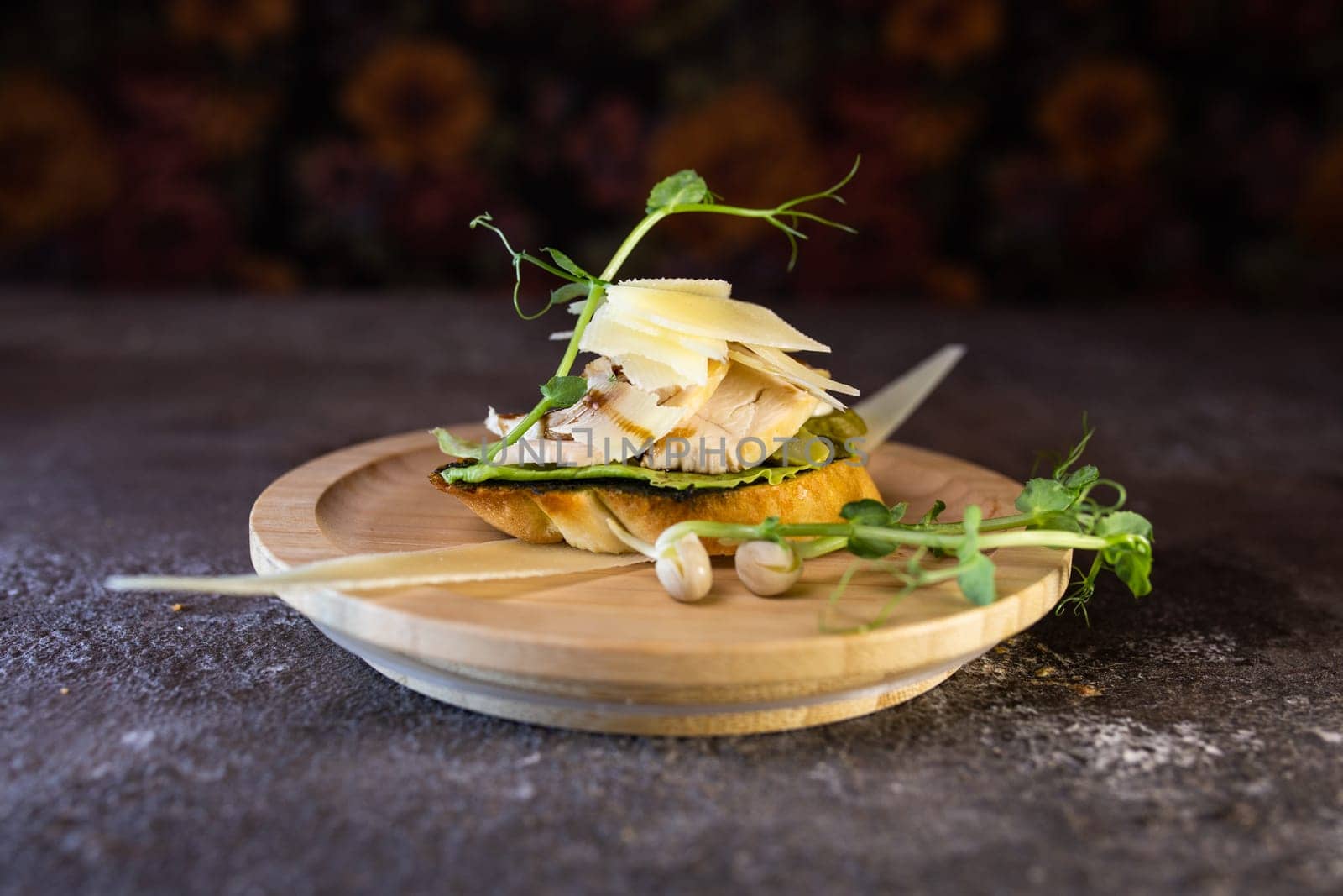 A delicious open-faced sandwich with tender chicken, melted cheese, flavorful pesto, and fresh microgreens on a wooden plate. Perfect for a quick and satisfying lunch or dinner.