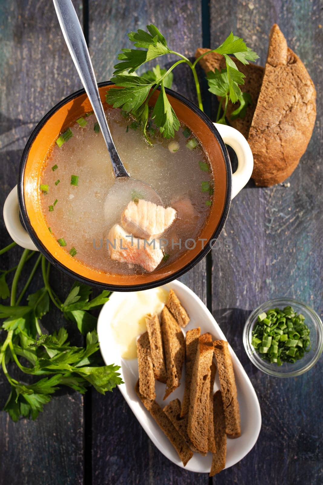 Close-up of a bowl of fish soup with fresh herbs and bread on a wooden table. by Pukhovskiy