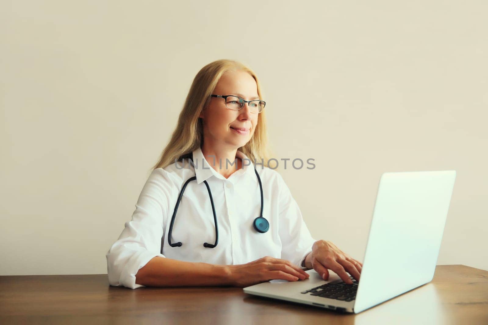 Caucasian middle-aged woman doctor working with laptop computer while sitting at desk in medical clinic office