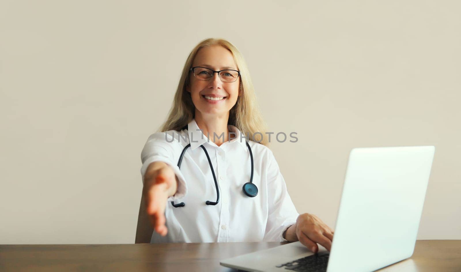 Caucasian middle-aged woman doctor working with laptop computer while sitting at desk in medical clinic office