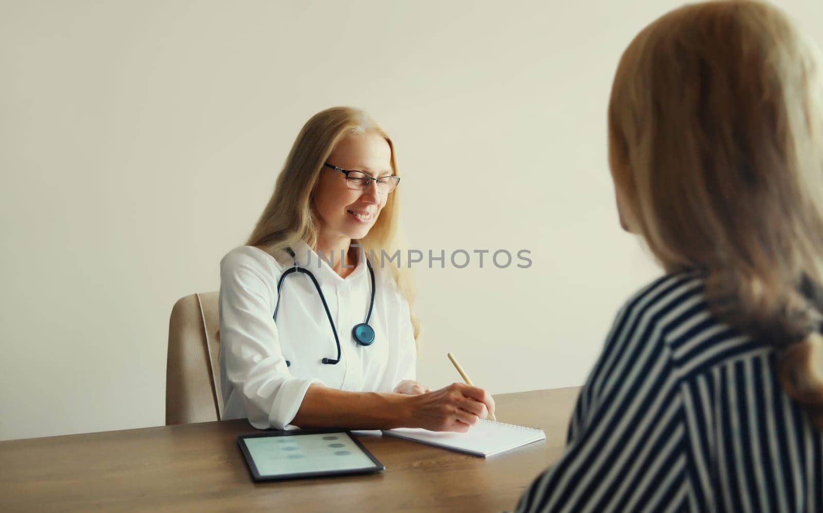 Patient at doctor's appointment. Caucasian middle-aged woman doctor therapist talking to the girl prescribes medications while sitting at table in clinic office
