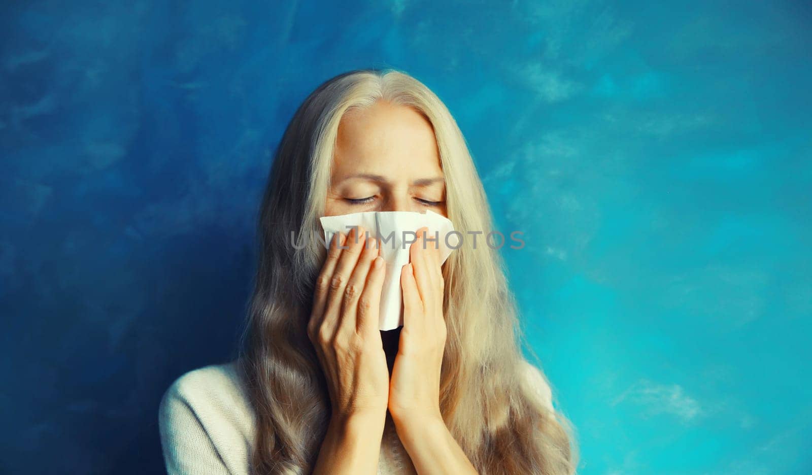 Sick exhausted middle-aged woman sneezing blow nose using tissue at home