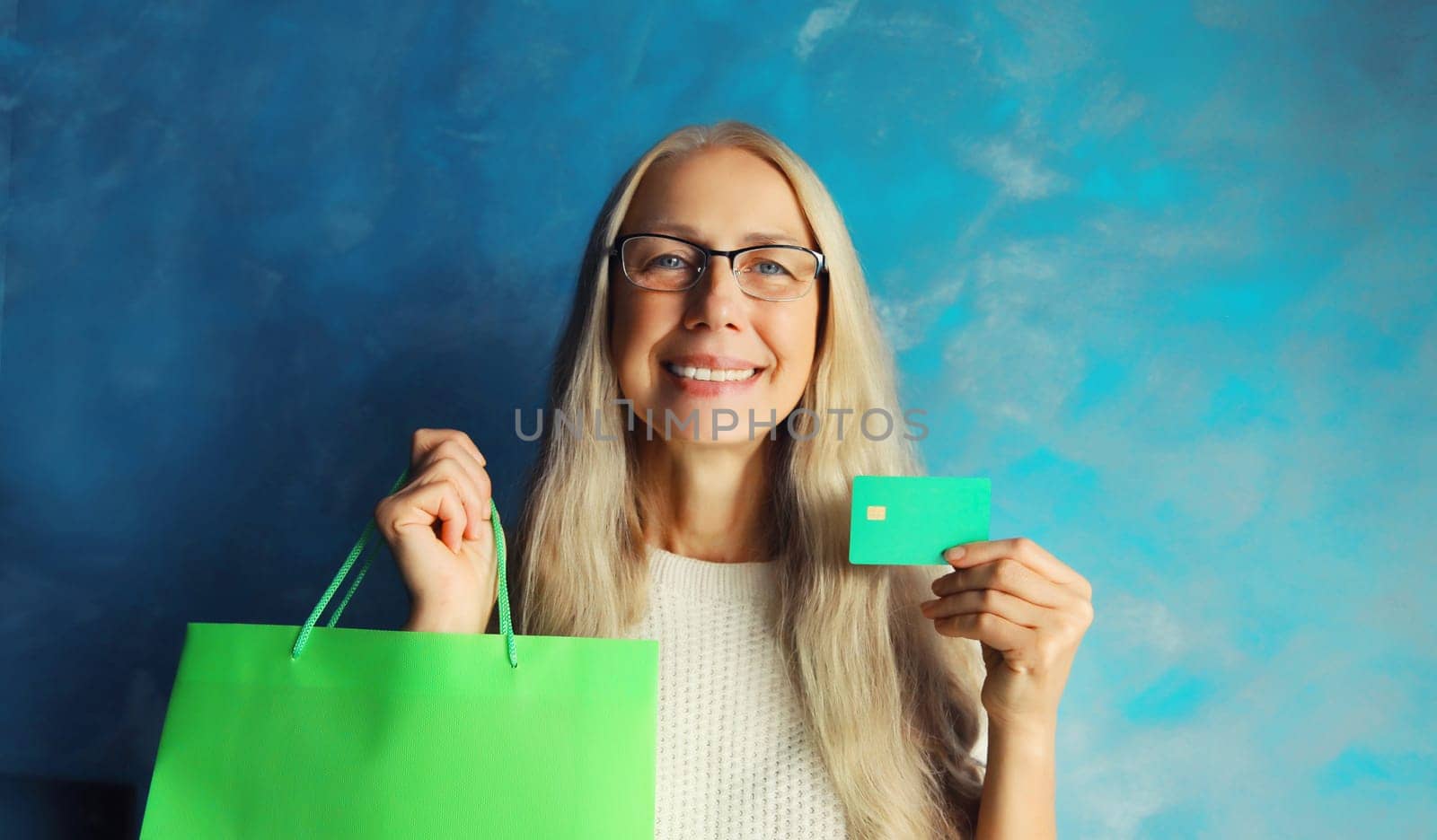 Portrait of happy smiling caucasian middle aged woman holding plastic credit bank card with shopping bags on studio background