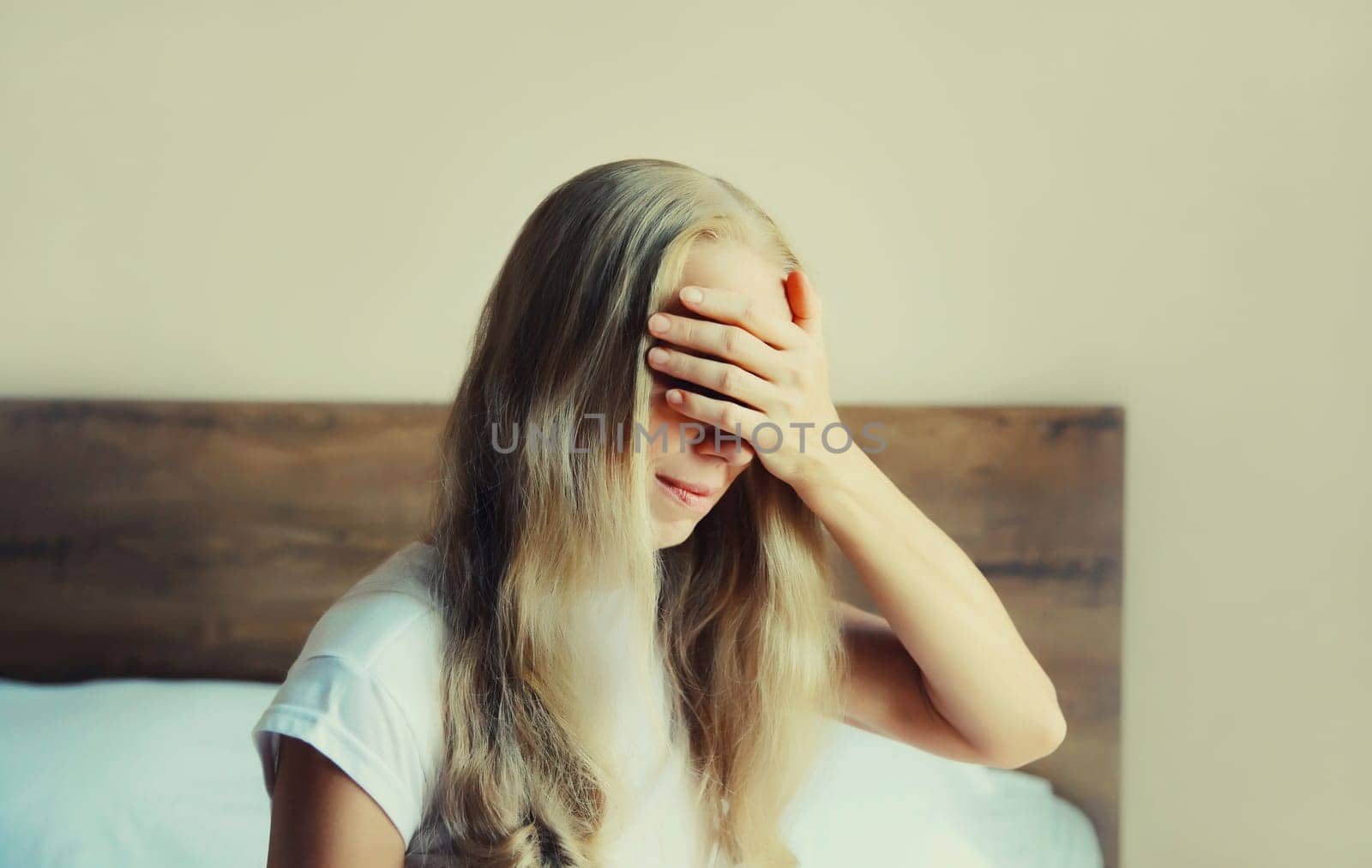 Upset sad crying woman covering her eyes with hands on the bed experiencing mental suffering in bedroom at home