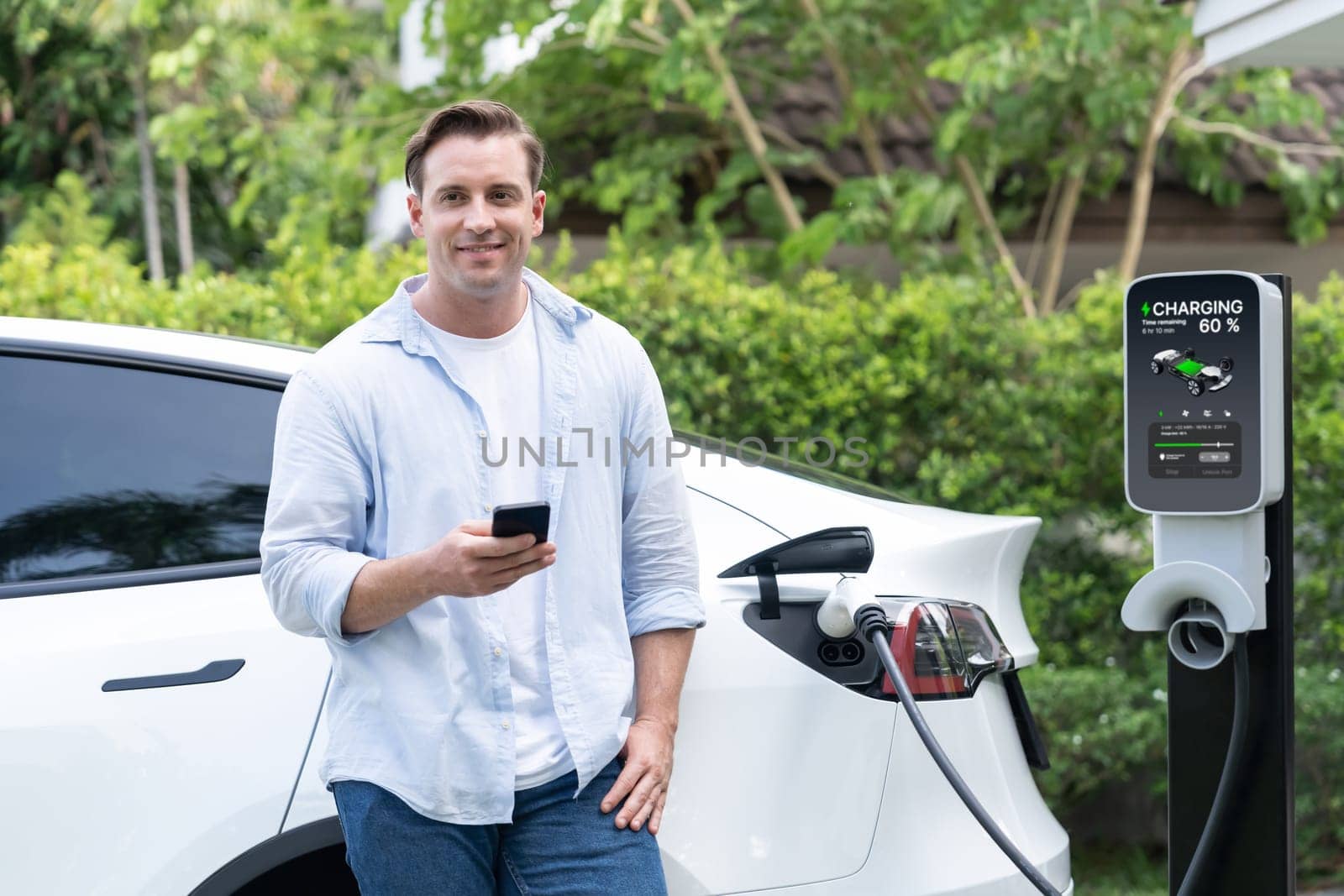 Modern eco-friendly man recharging electric vehicle from home EV charging station. Innovative EV technology utilization for tracking energy usage to optimize battery charging at home. Synchronos