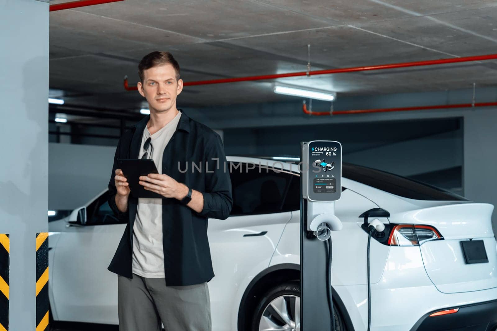 Young man travel with EV electric car to shopping center parking lot charging in downtown city showing urban sustainability lifestyle by green clean rechargeable energy of electric vehicle innards