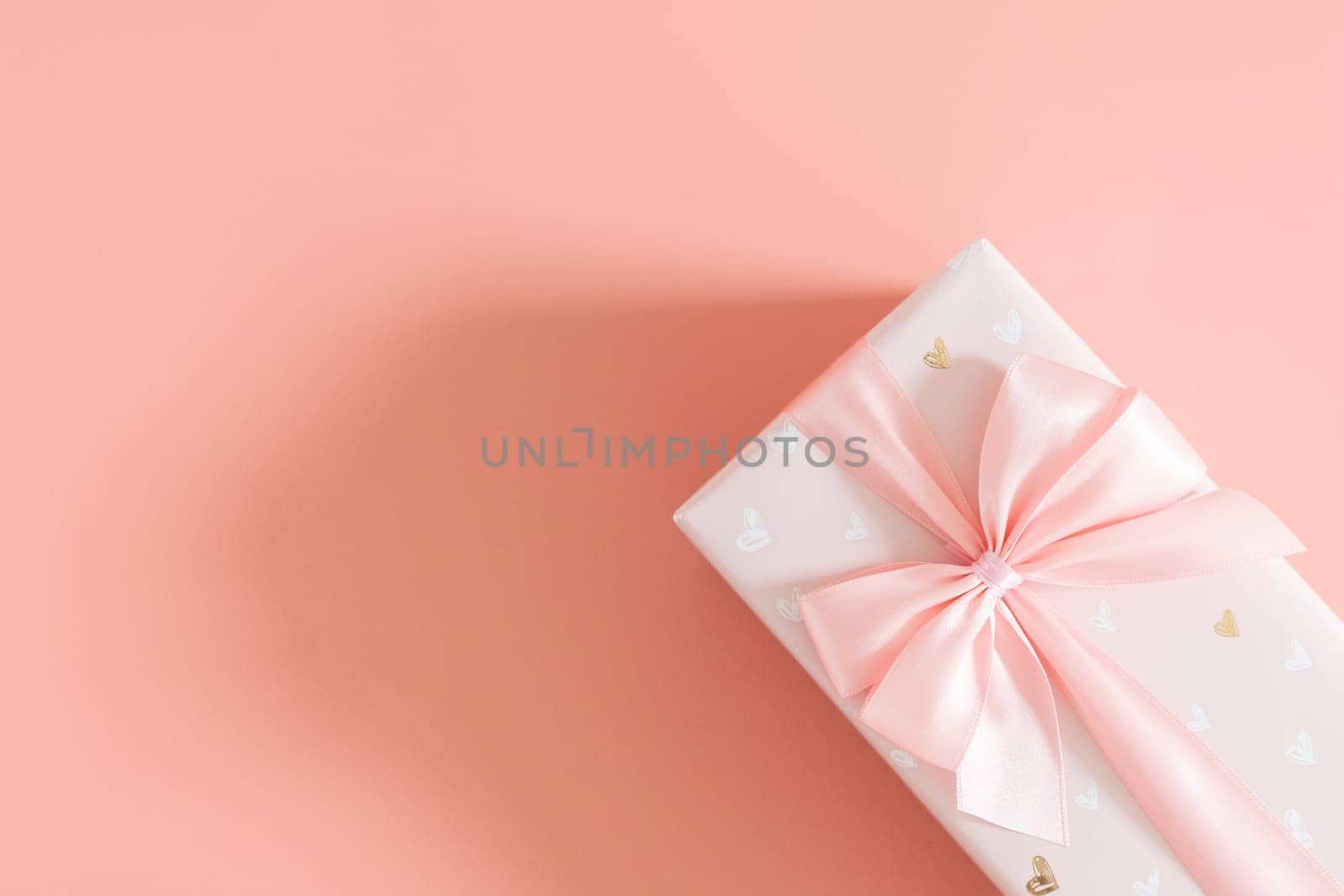 One beautiful gift box with a bow lie on the right on a pale pink background with copy space on the left, flat lay close-up.