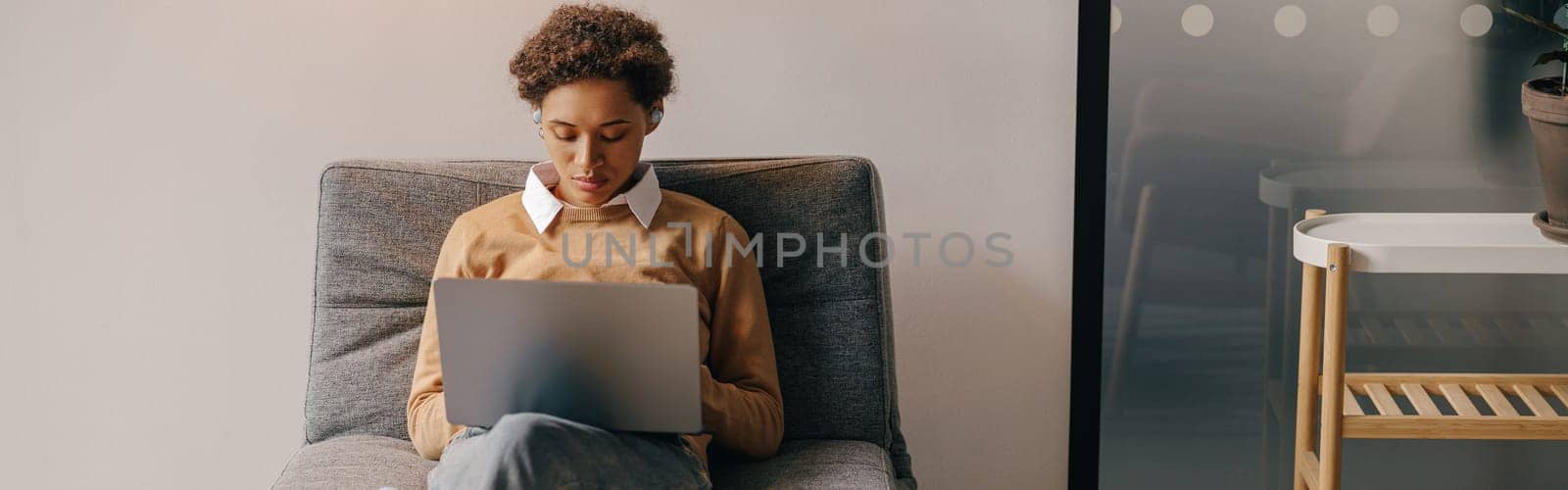 Pretty female freelancer working on laptop while sitting on modern coworking background