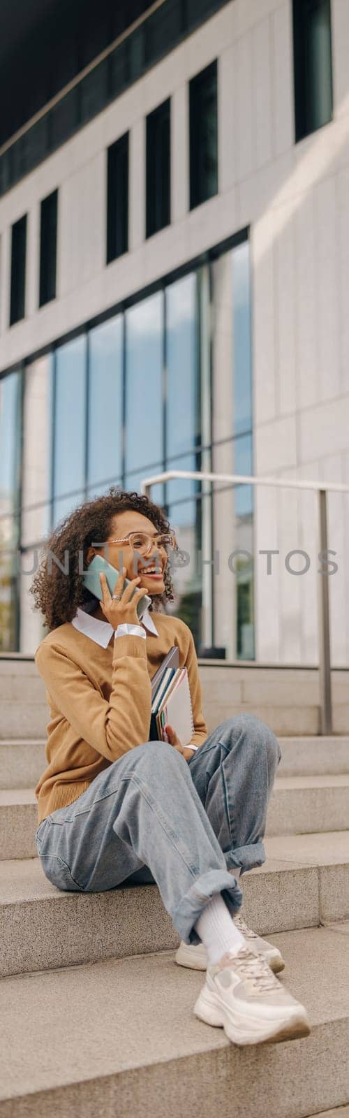 Cheerful business woman talking phone with client while sitting on stairs on building background