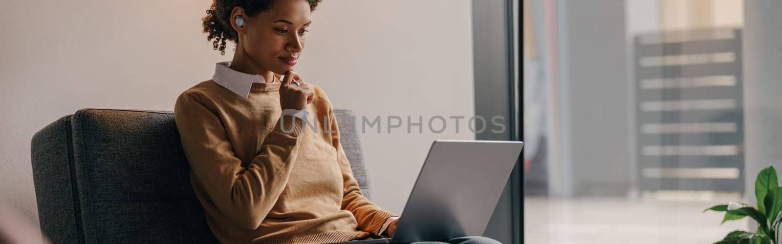 Pretty female freelancer working on laptop while sitting on modern coworking background