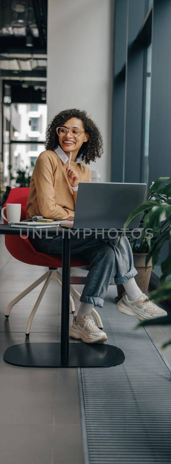 Business woman in eyeglasses working on laptop while sitting in modern office near window