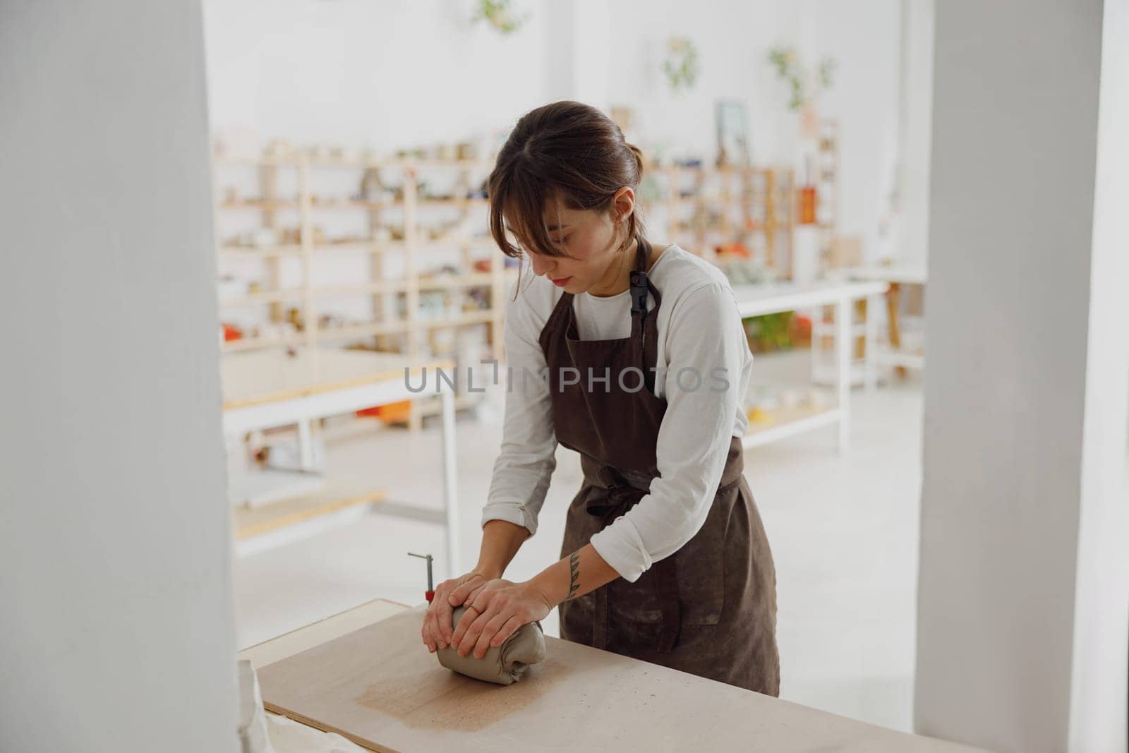 Pretty woman preparing clay to create a mug on a wooden table in pottery studio by Yaroslav_astakhov