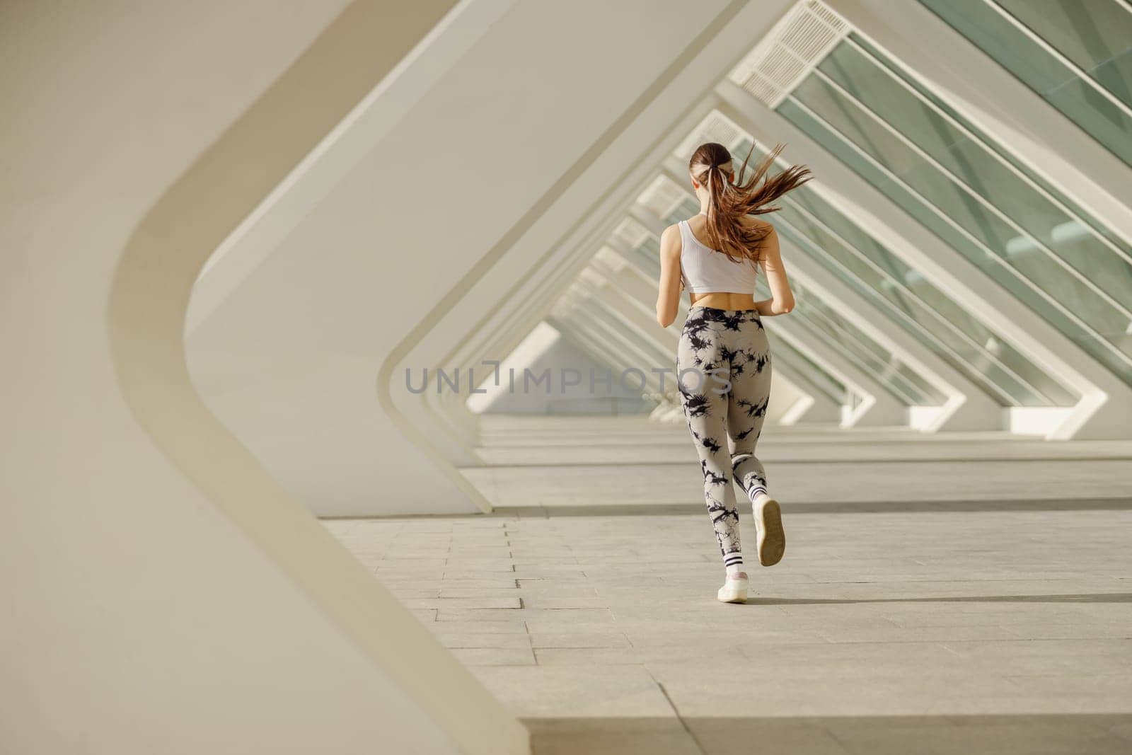 Back view of woman athlete is jogging on morning on modern building background. Healthy life concept by Yaroslav_astakhov