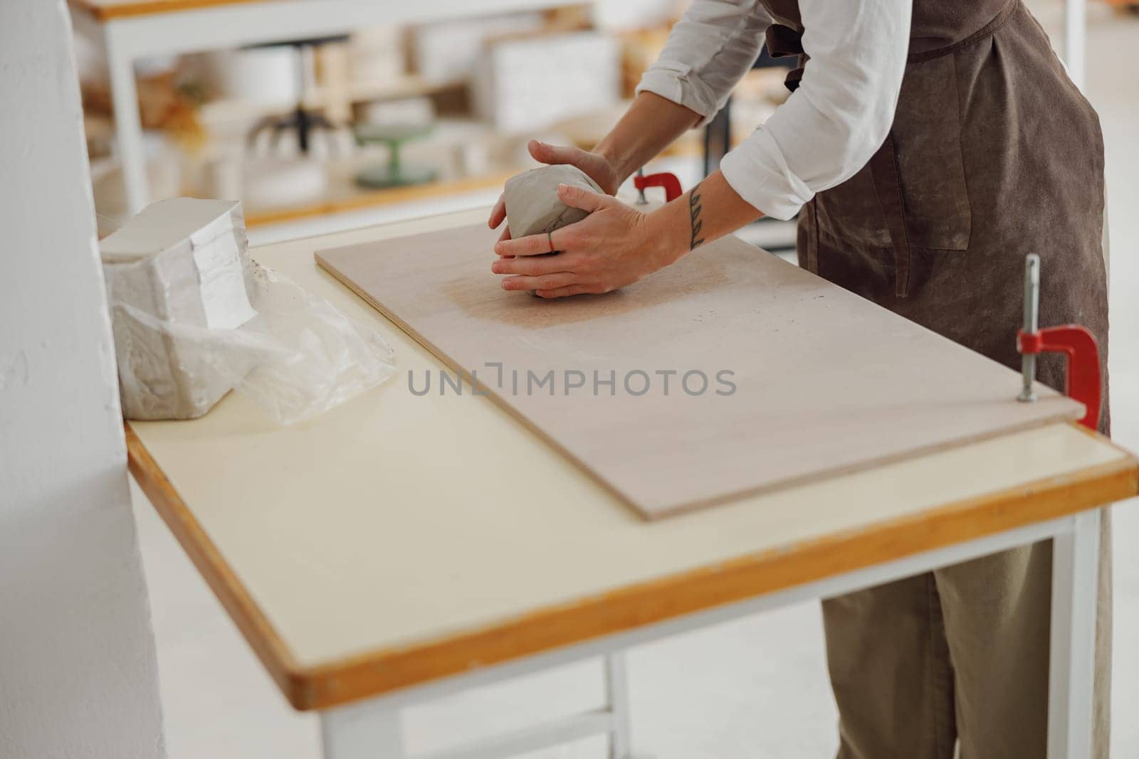 Close up of woman preparing clay to create a mug on a wooden table in pottery studio
