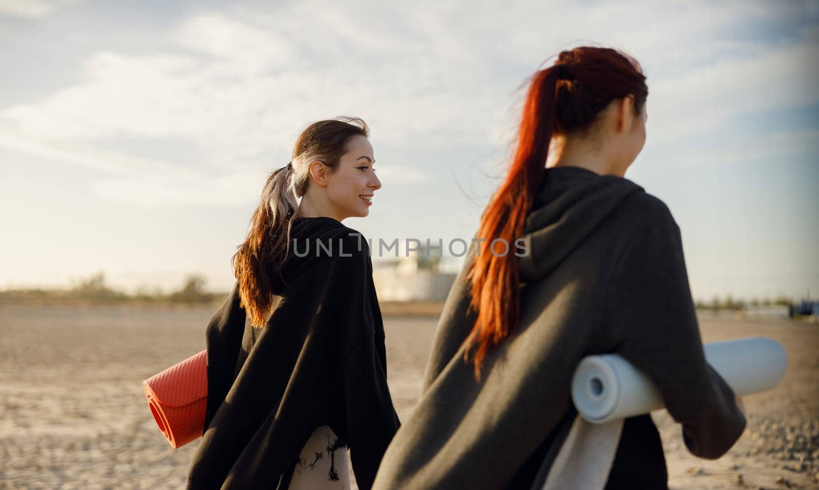 Two fit women walking on the beach with their yoga mats after doing morning gym. High quality photo