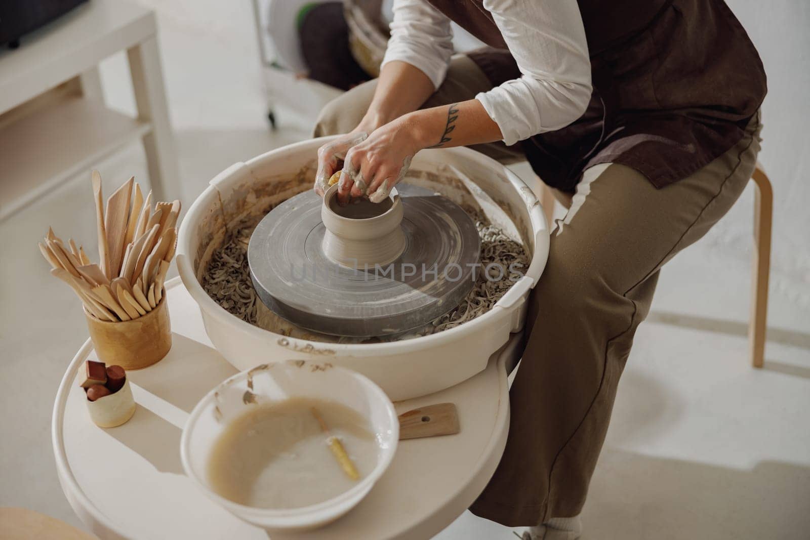 Female potter in apron making shape of clay vase on spinning pottery tool in ceramic workshop by Yaroslav_astakhov