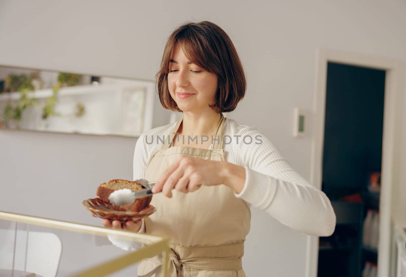 Pretty female waitress hands putting a delicious dessert on a plate standing behind bar counter by Yaroslav_astakhov