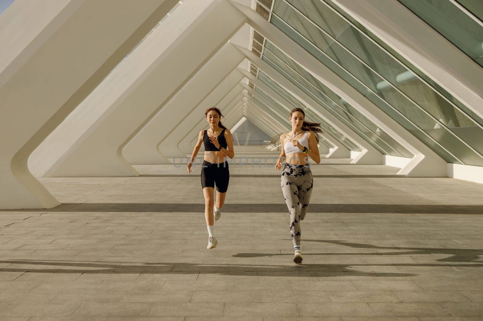 Two athletic women in sportswear is jogging around the city in early morning. Reaching the goal