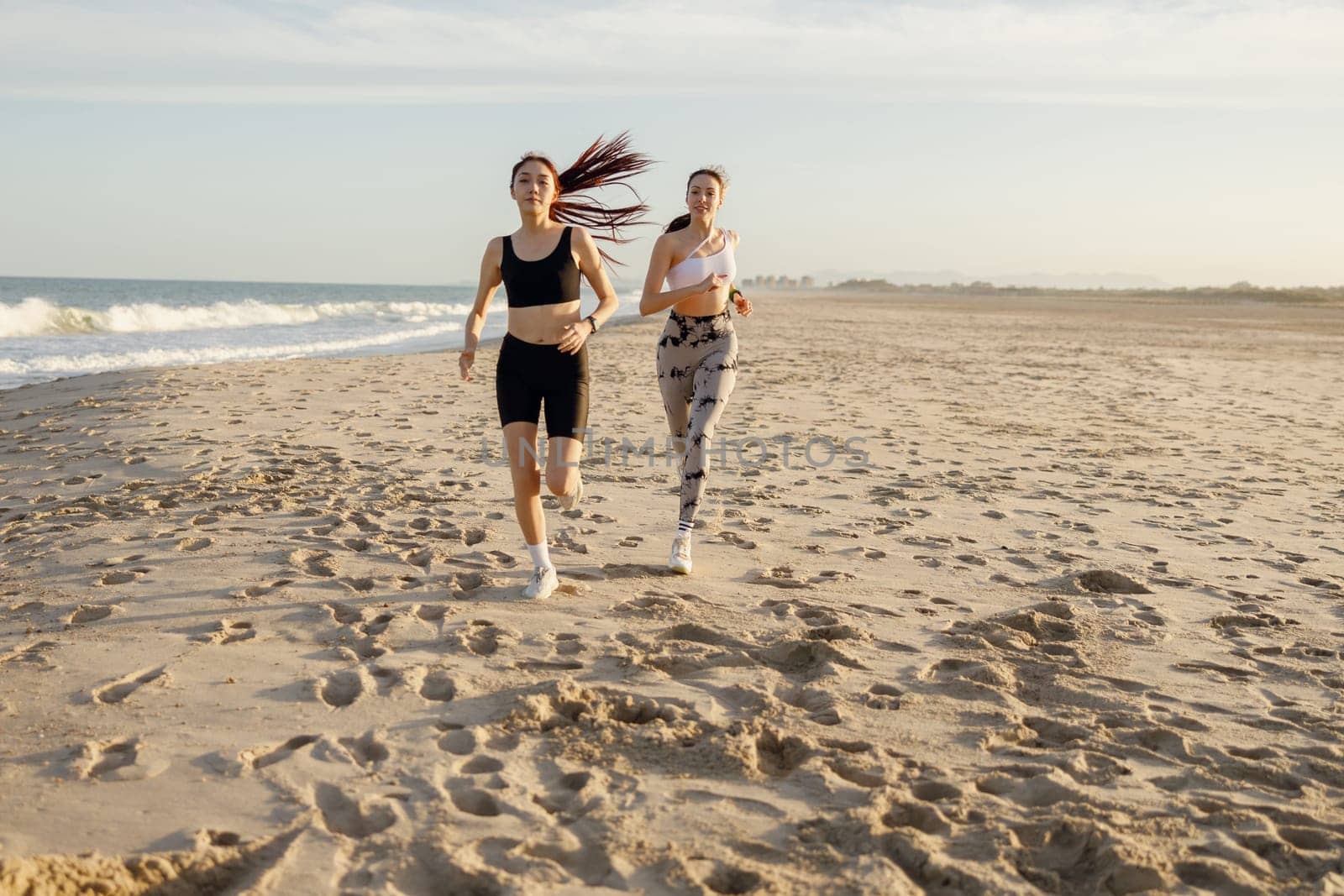 Young athletic women in sportswear is jogging along shore of beach. Concept of healthy living