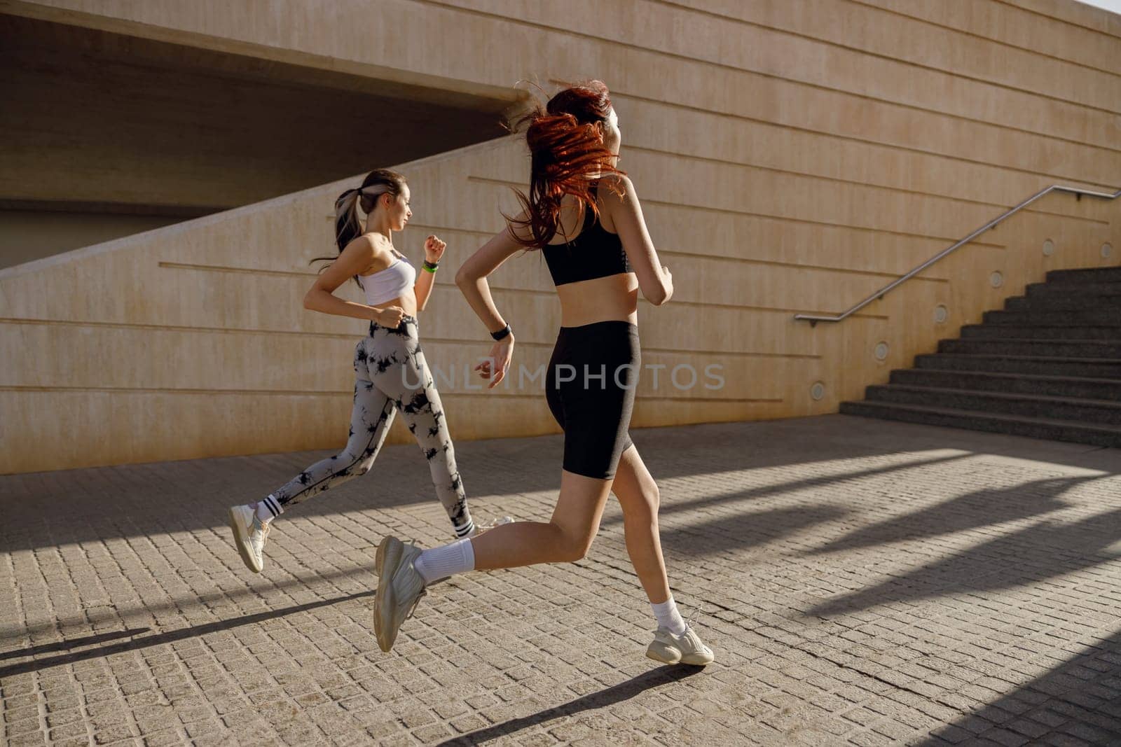 Side view of women athlete running side by side along an outdoor track on buildings background by Yaroslav_astakhov