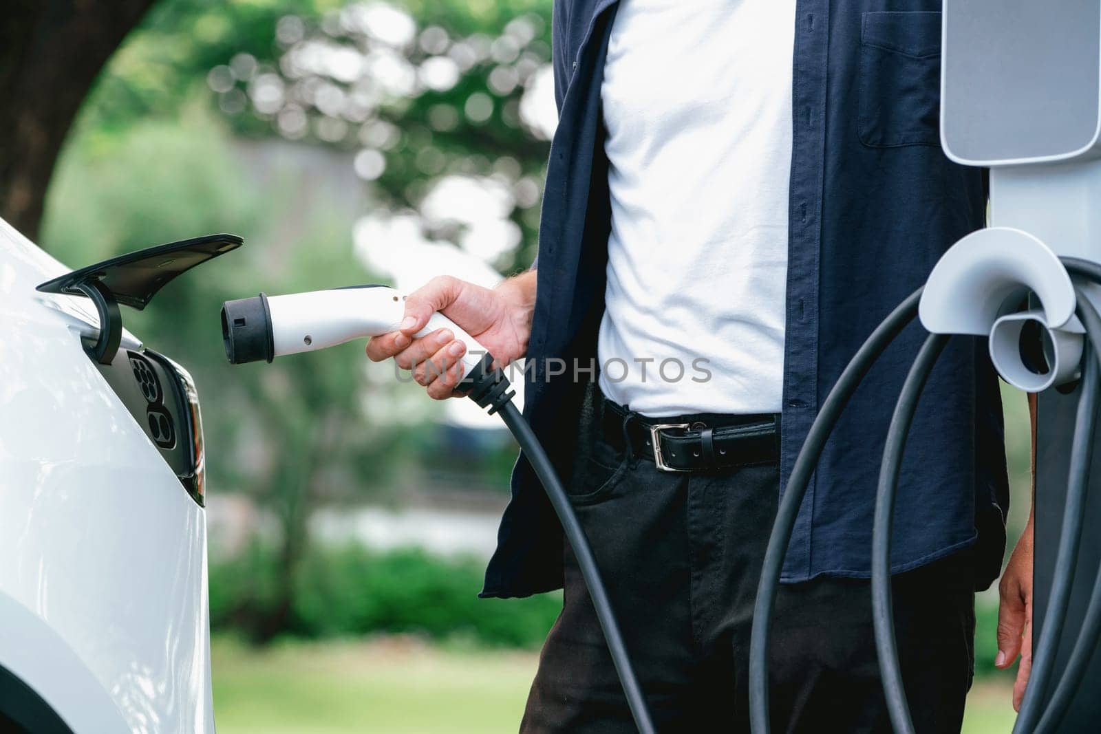 Man recharging battery for electric car during road trip. Exalt by biancoblue