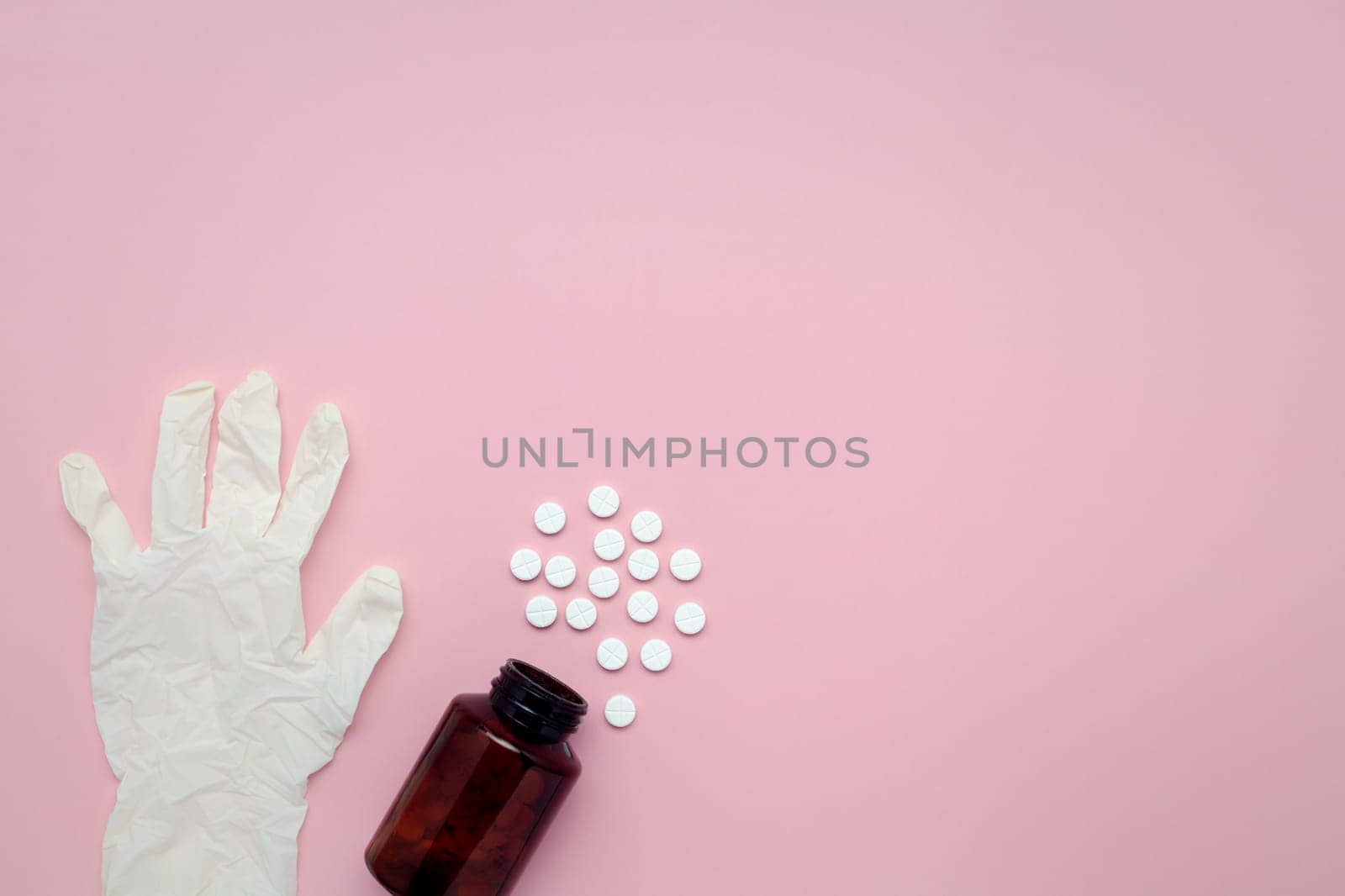 Flat lay of a bottle of medicine, pills, and latex gloves on a pink background for the concept of medical and healthcare