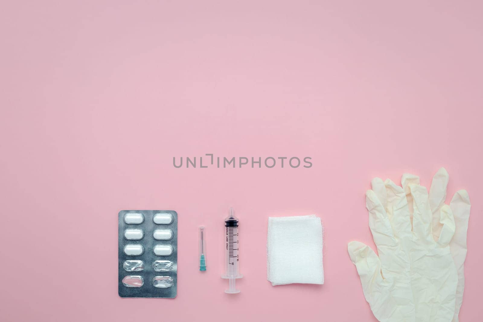 Flat lay of medication blister packs, syringes, gauze, and latex gloves on a pink background for the concept of medical and healthcare