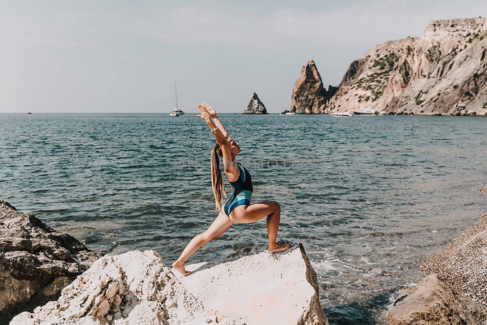 Yoga on the beach. A happy woman meditating in a yoga pose on the beach, surrounded by the ocean and rock mountains, promoting a healthy lifestyle outdoors in nature, and inspiring fitness concept