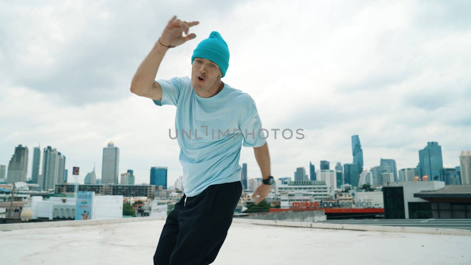 Caucasian B-boy dancer practicing street dancing at rooftop with city urban view. Motion shot of young man performing street dance by moving with hip -hop music. Outdoor sport 2024. Endeavor.